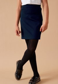 Granatowa dopasowana spódnica z elastycznego materiału, zestawiona z czarnymi rajstopami i błyszczącymi czarnymi loafersami z ozdobnymi frędzlami.