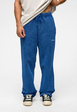 Blauwe fleece joggingsbroek met een elastische tailleband en trekkoord. Voorzien van een wit logo op de linkerdij en een ruime pasvorm.