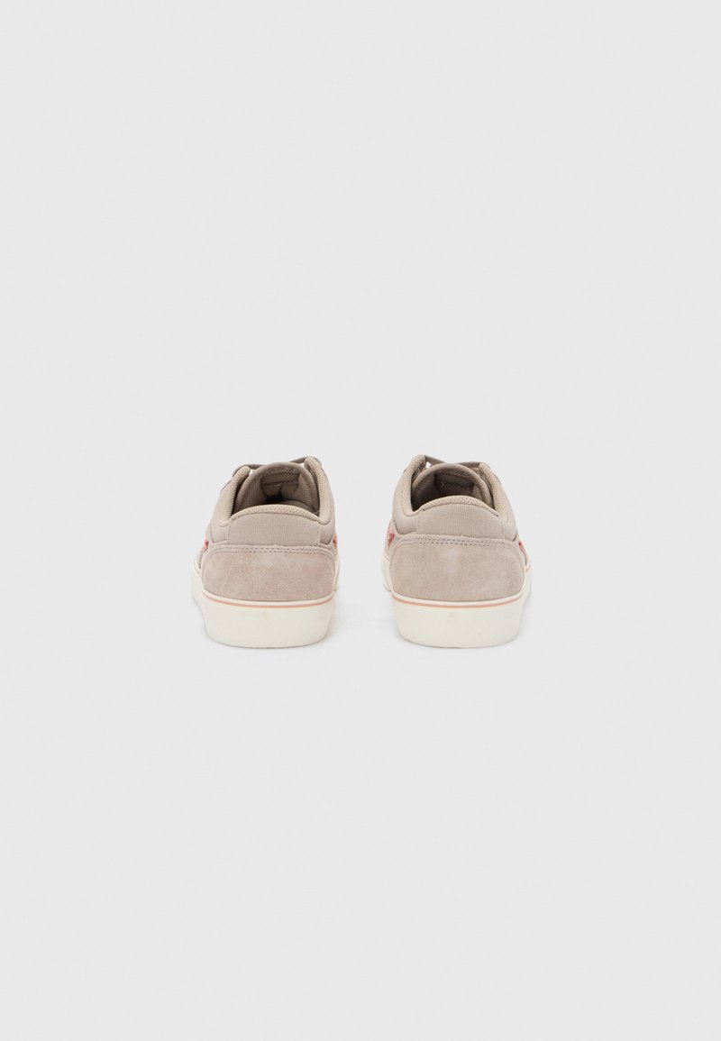 Beżowe zamszowe sneakersy o miękkiej fakturze, niskim profilu i kontrastujących białych podeszwach. Posiadają subtelne czerwone akcenty w okolicy pięty.