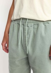 Lichtgroene corduroybroek met een elastische tailleband, voorzien van een trekkoord. De textuur is ribbelig, met verticale lijnen.