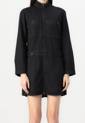 Černé džínové šaty s vysokým límcem, předním zipem, dvěma náprsními kapsami a bočními kapsami. Má přiléhavý pas zdobený knoflíkovými detaily.