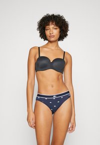 Melnas polsterētas krūšturis ar regulējamiem siksniņām; kombinēts ar tumši ziliem apakšbiksēm ar baltu Lacoste logotipu un maziem baltu rakstu akcentiem.