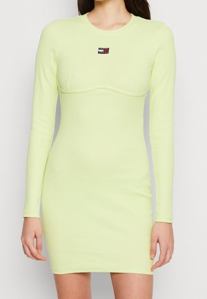 Mujer que lleva un minivestido ajustado de manga larga, de color verde claro, con un pequeño logo de Tommy Jeans en el pecho.