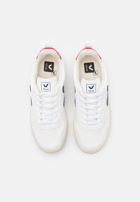 Sneakers bianchi in pelle perforata, con accenti laterali blu navy e un tab sul tallone rosso. Presentano lacci bianchi e un logo sulla linguetta.