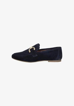 Marineblauwe suède loafer met goudkleurige metalen gesp en platte beige zool, zijaanzicht op witte achtergrond.