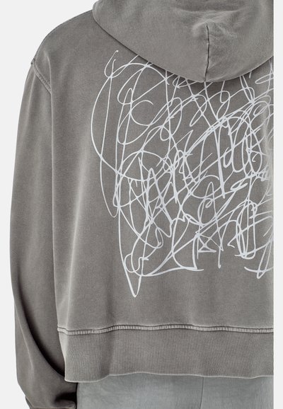 Grijze hoodie met een gestructureerde afwerking en een losse pasvorm. Heeft een witte krabbels grafiek op de achterkant en een geribde zoom bij de taille.