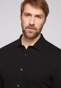 Zwarte poloshirt van een gestructureerde stof, met een klassieke kraag en drie knopen. Ontworpen voor een getailleerde pasvorm.