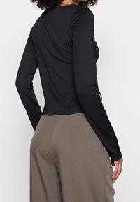 Top nero a maniche lunghe con un design aderente, realizzato in tessuto morbido. Abbinato a pantaloni larghi color marrone chiaro che mostrano una vestibilità rilassata.