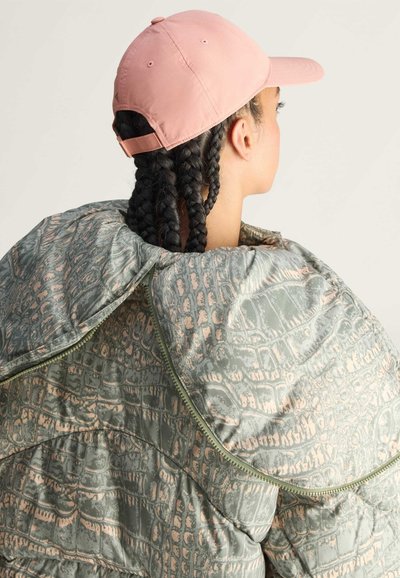 Pufferjas van textuurmateriaal in groen met een krokodillenpatroon en roze accenten. Het combineren van een lichtroze pet maakt de look compleet.