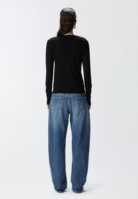 Top a maniche lunghe nero a costine abbinato a jeans in denim azzurro chiaro svasati, con due tasche posteriori e una vestibilità comoda.