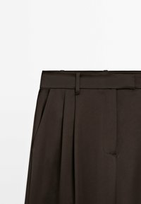 Brown pleated trousers with a wide waistband, featuring a side pocket and a smooth, textured fabric. Tailored design with belt loops.