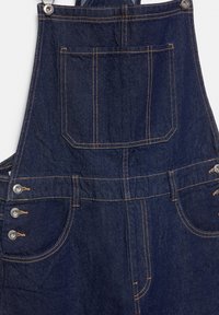 Detail tmavomodrých denimových overalov s predným náprsným vreckom, bočnými gombíkmi a kontrastným oranžovým prešitím.