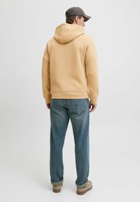 Sudadera beige con capucha ajustable, corte relajado, bolsillo canguro y puños acanalados, combinada con jeans de color azul claro y calzado beige.
