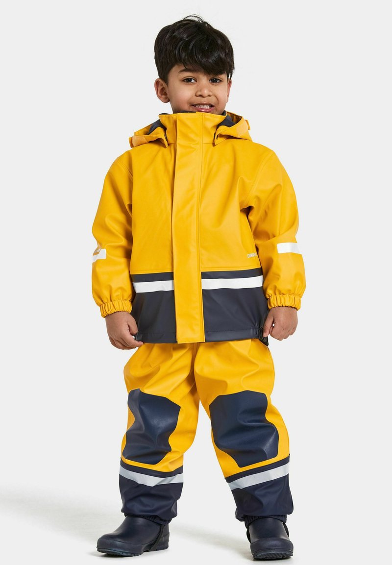 Geel waterdichte regenjas en broek met marineblauwe accenten, voorzien van witte reflecterende strepen en elastische manchetten; rubberen laarzen maken de outfit compleet.