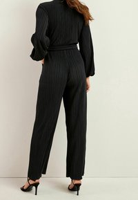 Zwart gestreepte jumpsuit met lange, opgeblazen mouwen. Heeft een getailleerde taille en wijde broekspijpen. Draagt het met zwarte hoge hakken.
