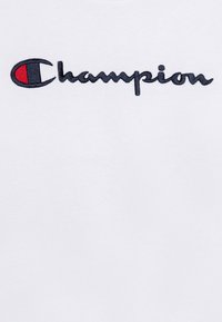 T-shirt in tessuto bianco con logo "Champion" ricamato in nero, con accenti rossi e blu sulla "C". Texture morbida, design classico.