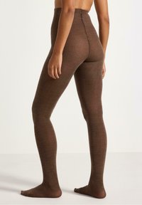 Brune ribbede leggings med høj talje og struktureret mønster, der fremviser et glat, tætsiddende design, som følger benenes konturer.