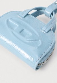 Malá lesklá svetlomodrá časť peňaženky s vyrazeným logom, dvojitým remienkom a viditeľným strieborným zipsom na neutrálnom pozadí.