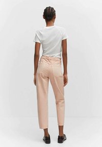 Pantalon en denim rose clair avec une taille haute et une coupe droite, doté de poches arrière, porté avec un t-shirt blanc à manches raglan et des chaussures noires.
