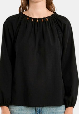 Blouse noire à manches longues avec un col froncé présentant de petits accents de perles en bois, portée avec un jean en denim bleu clair.