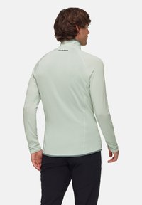 Light green fitted long-sleeve shirt with textured pattern, high collar, and flatlock seams. Features logo on the back neckline.