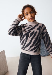 Fuzzy beige pullover sweater with black zebra stripes, high neck, and long sleeves, paired with dark gray jeans.