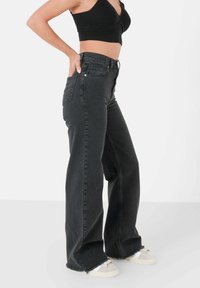 Zwart denim jeans met hoge taille en een rechte pijp, met een rafelige zoom en minimale hardware-details. Gecombineerd met lichtgekleurde sneakers.