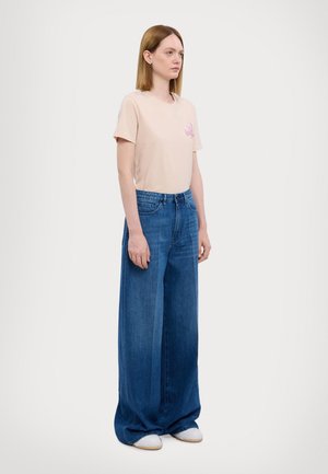 Light pink T-shirt with a small graphic, paired with oversized blue denim jeans and white sneakers. Smooth fabric and wide legs.
