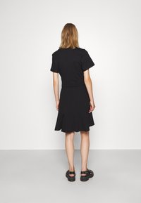 Czarna sukienka krótko rękawowa z rozkloszowanym dołem, wykonana z miękkiego materiału. Posiada skróconą górną część i jest zestawiona z masywnymi czarnymi sandałami.