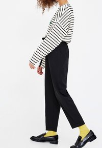 Chemise à rayures à manches longues en noir et blanc, pantalon noir, chaussettes jaunes et mocassins noirs ; présente une coupe décontractée et un design simple.