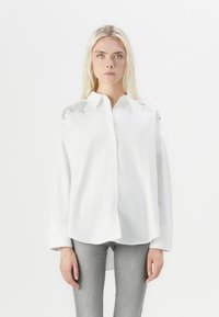 Cămașă albă cu guler clasic, având accente de argint texturat pe umeri și mâneci lungi lejer fitting.
