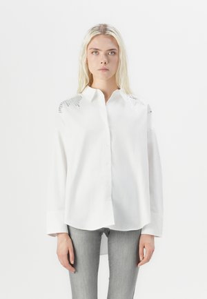 Camicia bianca con colletto classico, caratterizzata da accenti in argento texture sulle spalle e maniche lunghe morbide.