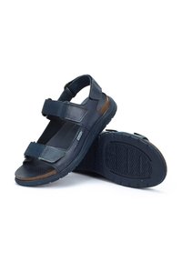 Sandalias azul marino con correas ajustables de Velcro, suela texturizada y un panel resaltado en marrón. Fabricadas en material sintético, cuentan con una plantilla para mayor comodidad.