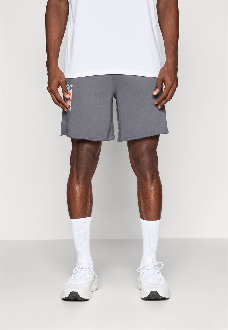 Graue Sportshorts mit einer Seitentasche und einem bunten Design, kombiniert mit weißen Knöchelsocken und hellen Sneakers auf einem neutralen Hintergrund.