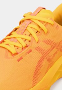 Chaussure de sport jaune vif avec un tissu texturé, des lacets oranges contrastants et un côté à motifs. Dispose d'une semelle rembourrée pour le confort.