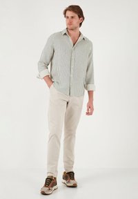 Camisa de botón a rayas en verde y blanco, chinos beige y zapatillas multicolores. Corte relajado, mangas largas y diseño de cuello abierto.
