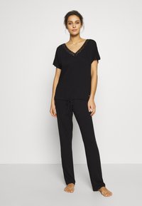 Black loungewear set featuring a short-sleeve top with a lace V-neck and drawstring pants. Soft fabric with a relaxed fit.