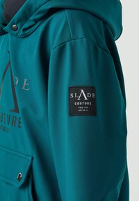 Felpa con cappuccio color teal realizzata in tessuto liscio con una grande stampa del logo, dotata di una tasca frontale e di un'etichetta patch nera sulla manica.