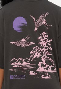 Δύο ροζ γερανοί πετούν κοντά σε ένα ροζ ορεινό τοπίο και δέντρο κάτω από ένα μοβ ήλιο, με το κείμενο "SAKURA Japanese Blossom" σε σκούρο ύφασμα.