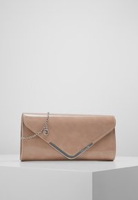 Béžová kožená obálková kabelka s stříbrným V- tvarem a tenkým stříbrným řetízkem na bílém podstavci na jednobarevném pozadí.