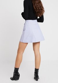 Ljusblå denim mini kjol med en figurnära midja, utställd nederkant och sidofickor, parat med svarta klackade ankelskor.