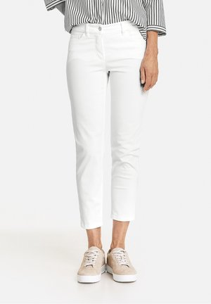 Pantalons en coton blancs, de longueur cheville et coupe slim, associés à des baskets en daim beige. Le haut présente des rayures verticales noires et blanches.
