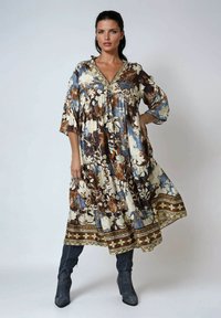 Robe à motifs floraux bleue, marron et crème avec un décolleté en V et des manches chauve-souris. Présente un ourlet à motifs et une texture de tissu léger.