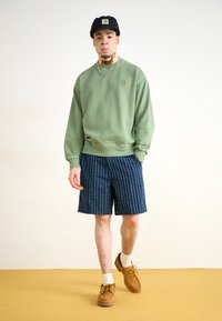 Grønn hettegenser, marineblå stripete shorts med hvite prikker, brune sko og en svart caps. Enkel design med teksturert stoff og synlig søm.