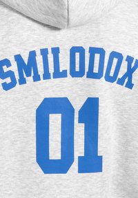 Felpa grigia con cappuccio caratterizzata da testo blu "SMILODOX" disposto ad arco sopra il numero "01" in un font bold sans-serif. La trama del tessuto è morbida e liscia.