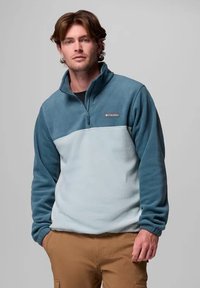 Pullover in pile blu e azzurro, con zip a un quarto, texture morbida e logo ricamato sul petto. Design semplice e funzionale.