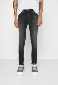 Jeans ajustados negros de mezclilla, con una sutil textura desvaída. Combinados con una camisa blanca y zapatillas grises. Presenta bolsillos estándar.