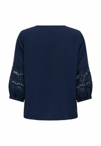 Blouse bleu marine en tissu texturé, avec des manches trois-quarts présentant des motifs en dentelle découpée et des poignets boutonnés.