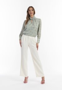 Blusa floreale blu chiaro con scollatura a chiave, abbinata a pantaloni bianchi a gamba larga. Tacchi a rocchetto rosa completano l'outfit.