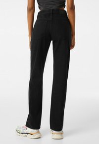 Jeans negros de talle alto hechos de denim, con piernas rectas, dos bolsillos traseros y una superficie texturizada, combinados con zapatillas multicolores.